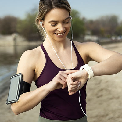 Young Woman Jogging Near River wearing headphones checking smart watch