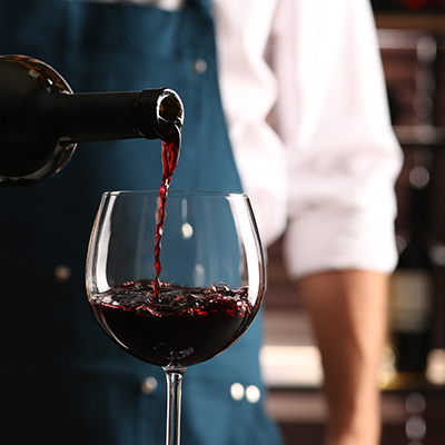 Bartender pouring red wine into glass indoors, closeup. Space for text