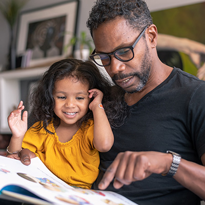 Affectionate father reading book with adorable mixed race daughter